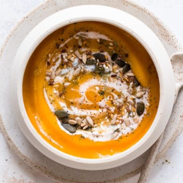 Vegan butternut squash soup with coconut milk and mixed seeds, served in a beige bowl