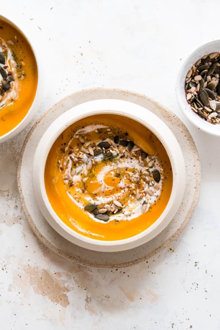 Vegan butternut squash soup with coconut milk and mixed seeds, served in a beige bowl
