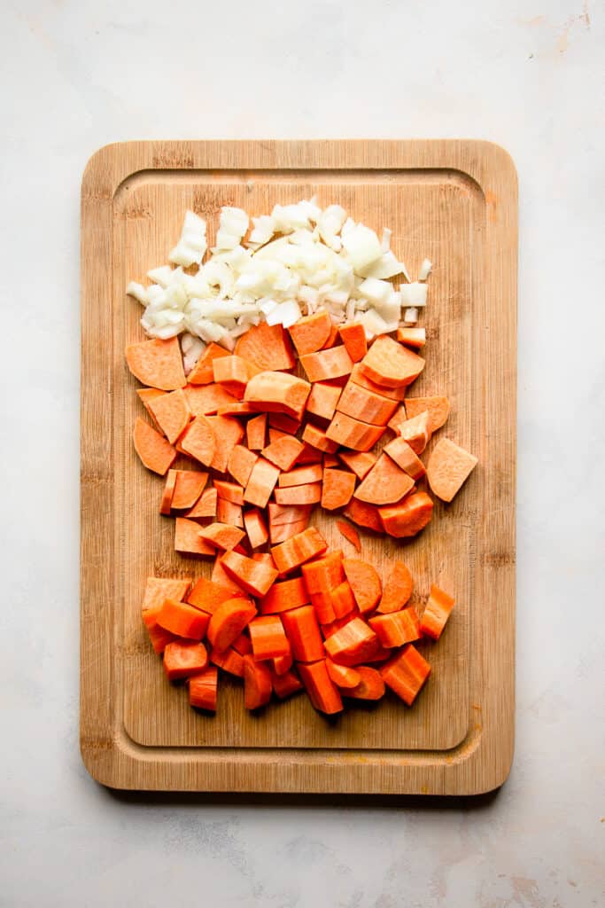 Chopped onion, carrots and sweet potato on a cutting board.