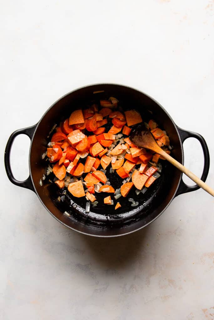 Sauteed onion, carrots and sweet potatoes in a black pot.