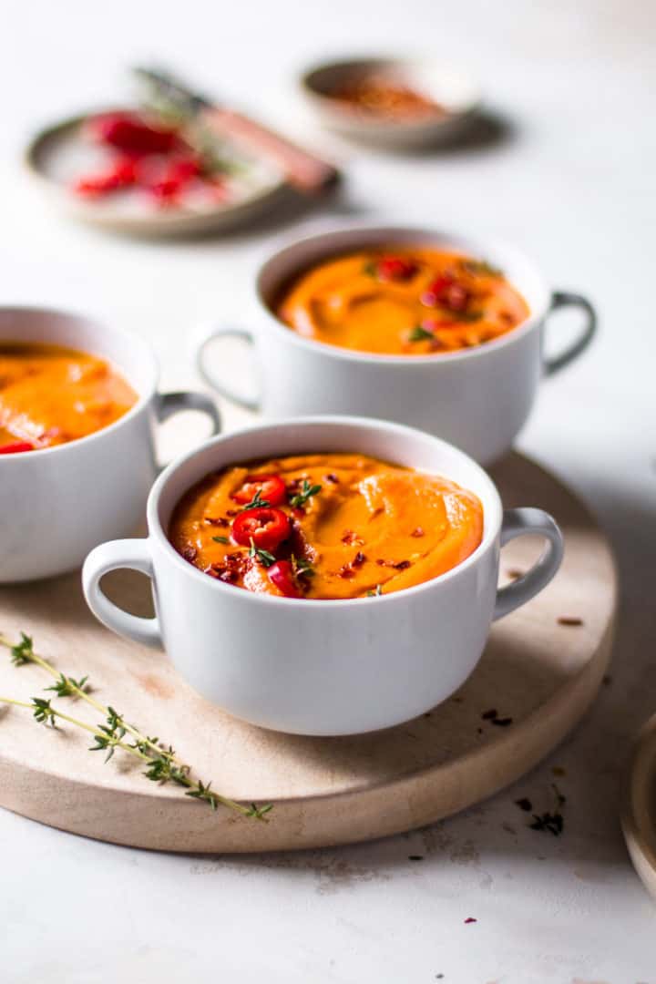 Three bowls of sweet potato and tomato soup on a wooden board.