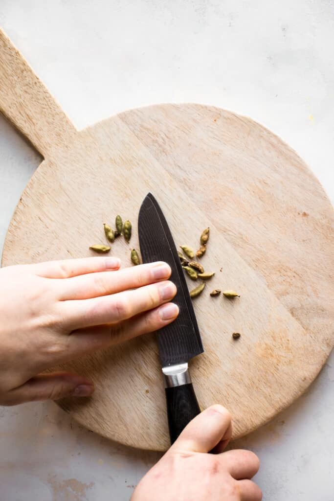 Crushing cardamom pods with the flat side of a knife.