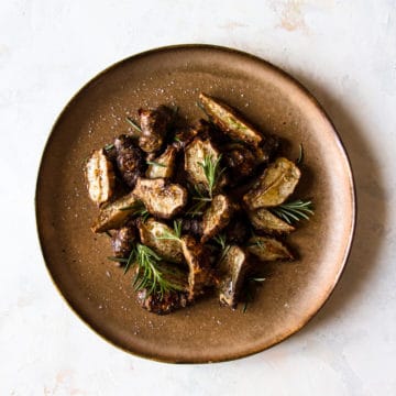 Rosemary roasted Jerusalem artichokes on a brown plate with fresh rosemary