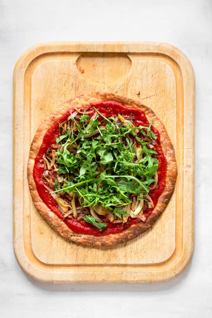 Baked pizza with red sauce, sauteed fennel topped with arugula.