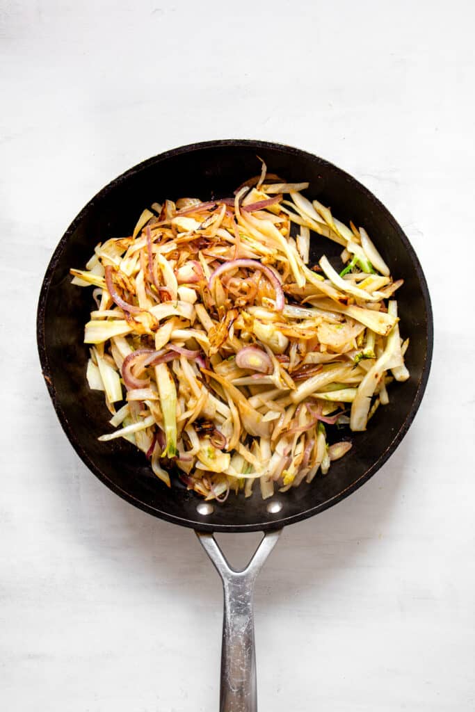 Sauteed fennel and onion in a black pan.