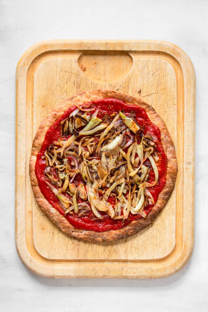 Pizza crust with added toppings on a large wooden board.