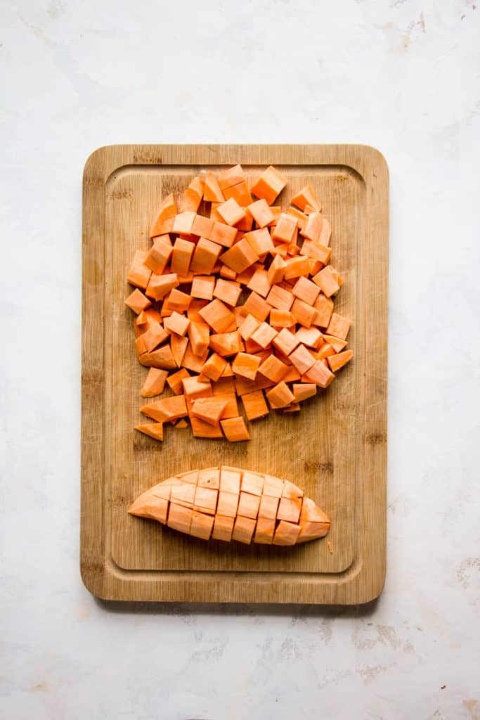 Sweet potatoes cut in cubes on a wooden cutting board