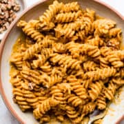 Pumpkin pasta in a bowl topped with walnuts.
