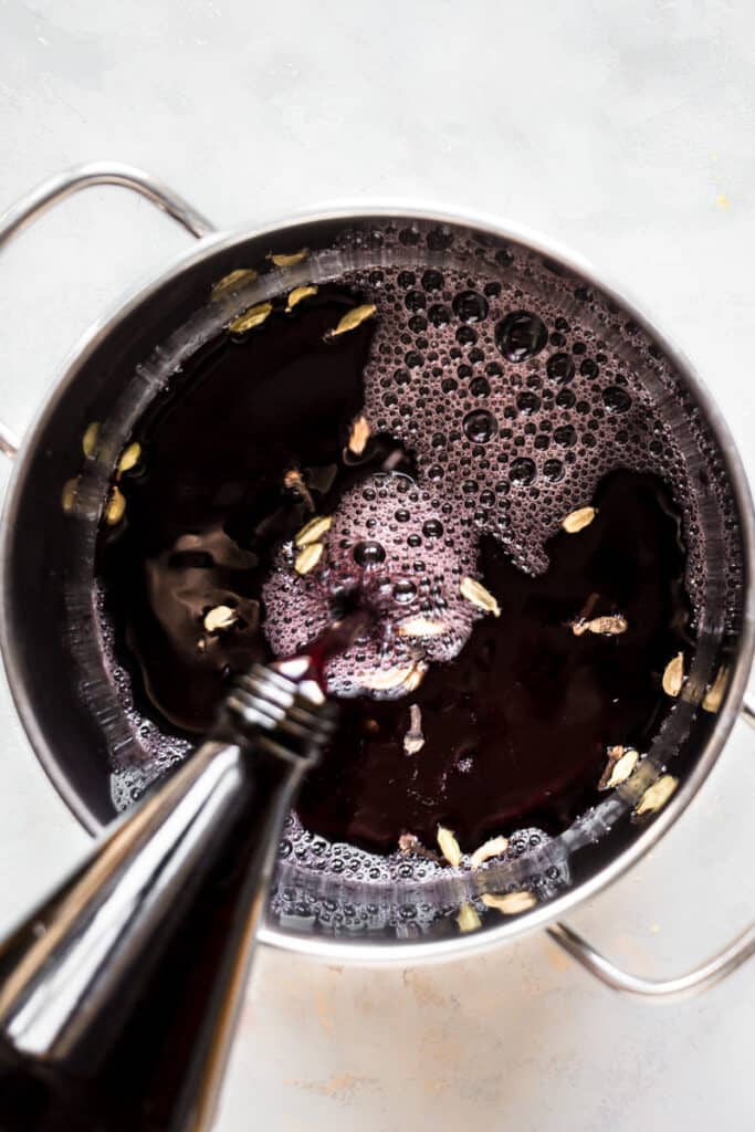 Pouring grape juice into the pot with spices.