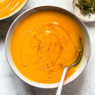 Bright orange soup in a grey ceramic bowl drizzled with olive oil.