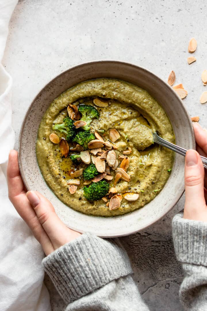 Hands holding a bowl of dairy-free broccoli soup.