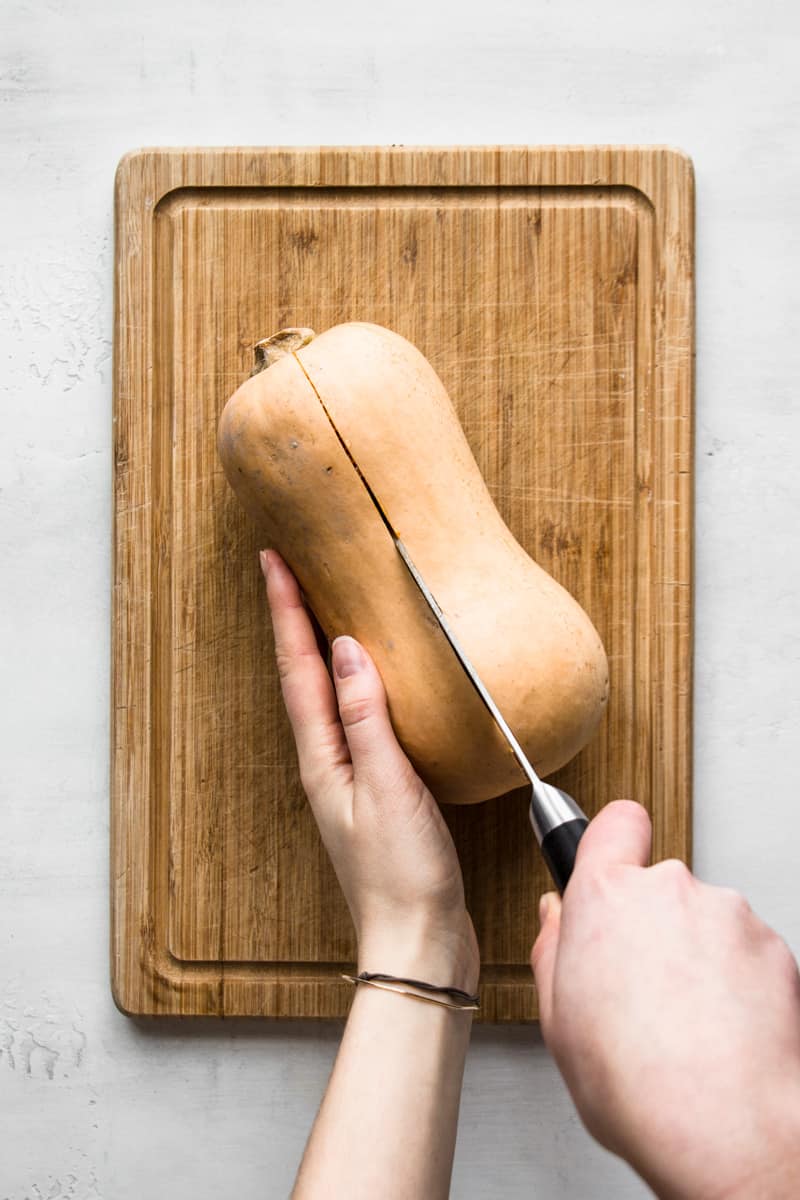 Hand cutting a butternut squash lengthwise in half.