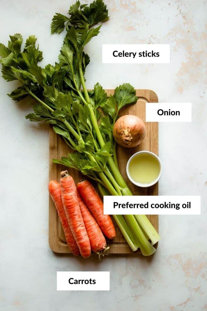 Celery, carrots, onion and oil on a cutting board.