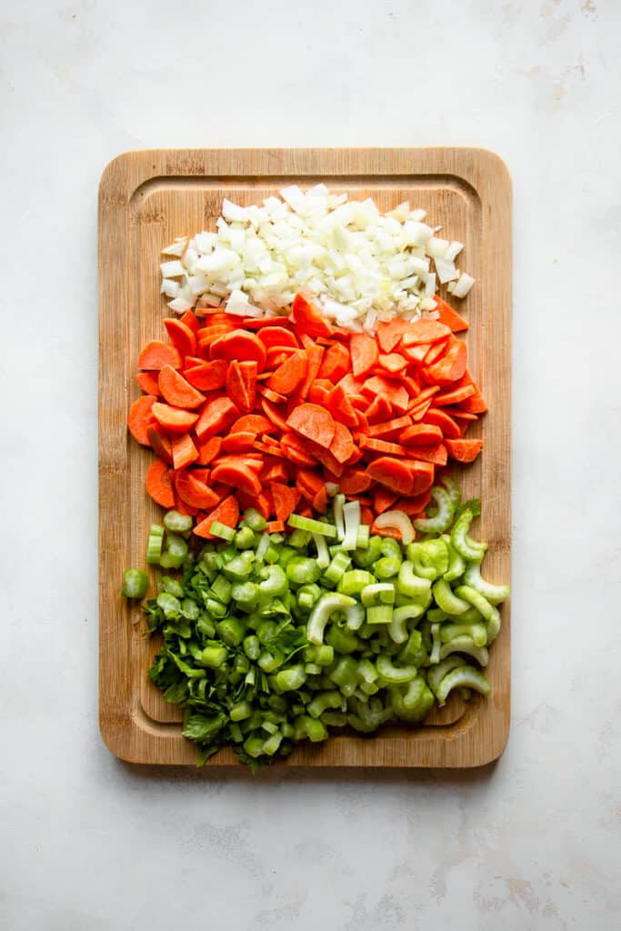 Chopped onion, carrots and celery on a cutting board.