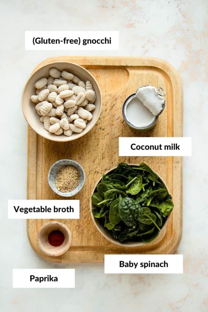 Gnocchi, coconut milk, spinach, vegetable broth and paprika on a cutting board.