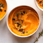 Bowl of butternut squash soup with pumpkin seeds and fresh thyme.
