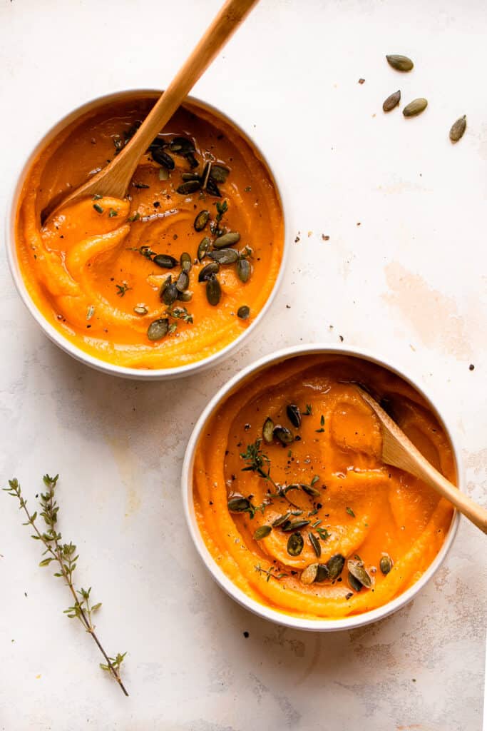 Two bowls of 3-ingredient butternut squash soups with bamboo spoons in it.
