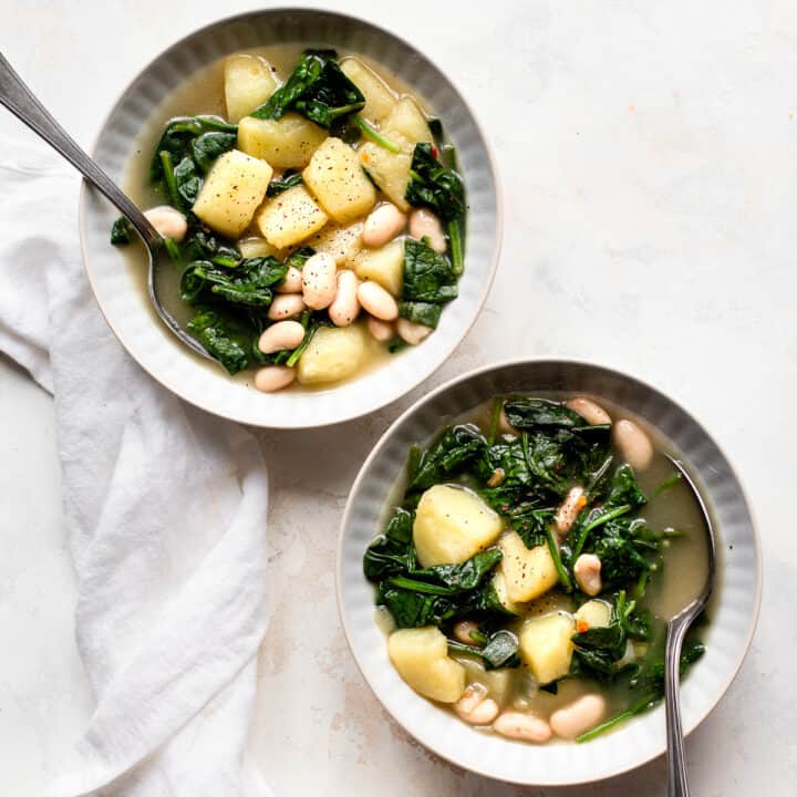 Two bowls of vegan spinach soup with potatoes and white beans.