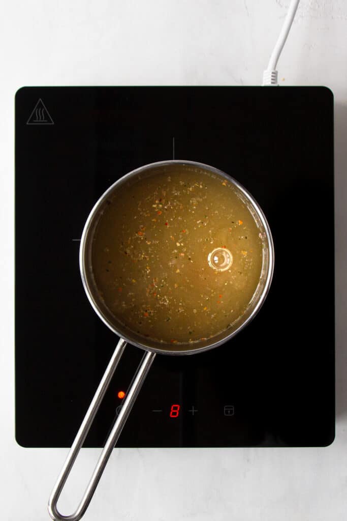 Small saucepan with vegetable broth on a cooking plate.