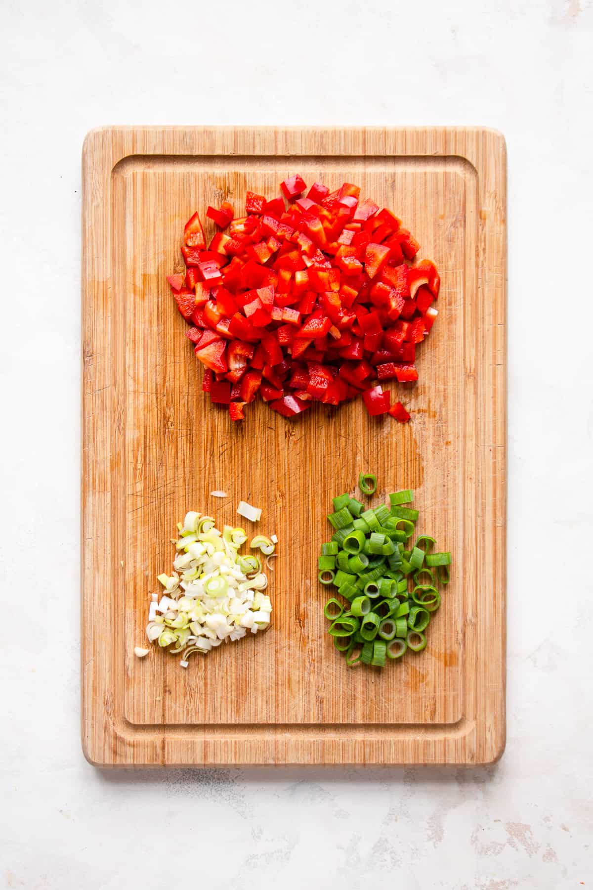 Chopped red pepper and scallions on a wooden cutting board.