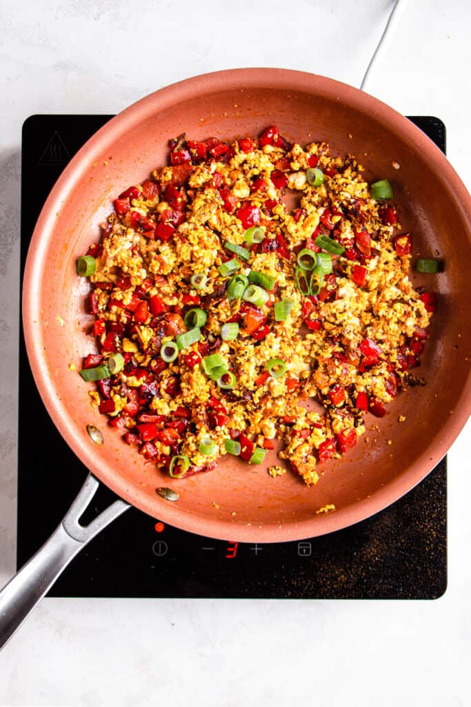 Silken tofu scramble in a pan with red peppers and scallions.