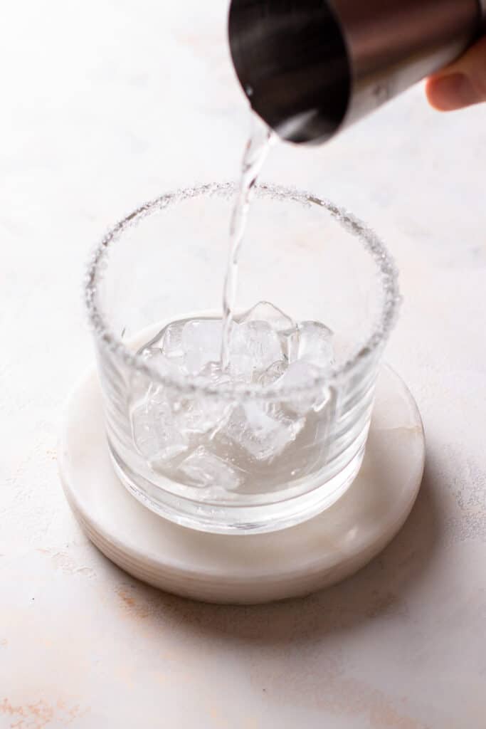 Hand pouring gin in a sugar rimmed glass.