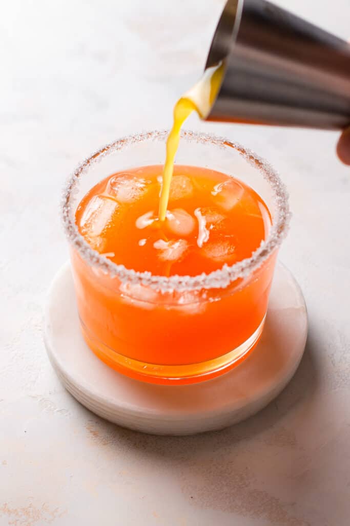 Hand pouring orange juice in a sugar rimmed glass.