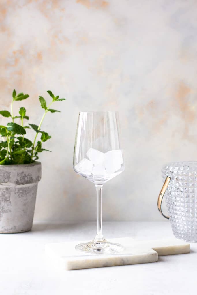 Wine glass filled with ice cubes and a mint plant in the background.