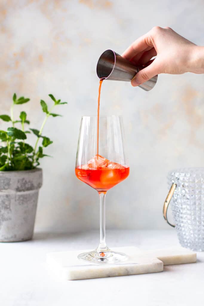 Hand pouring Aperol into the wine glass.
