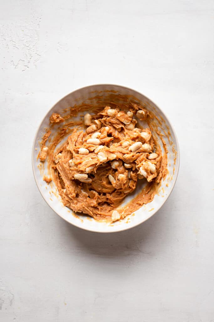 Peanut butter and whole peanuts in a medium bowl.