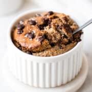 Baked oats with chocolate chips in a small white ramekin on a white marble coaster.