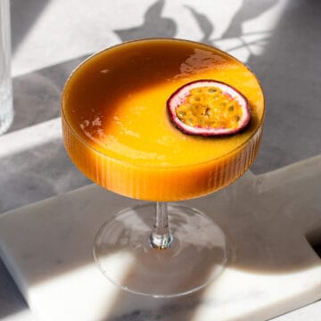 Coupe glass filled with orange cocktail and garnished with half a passion fruit.