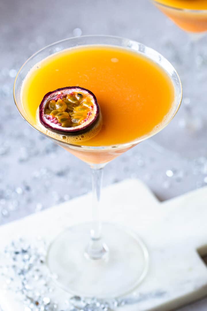 Half a passion fruit placed on a bright orange drink in a V-shaped glass.