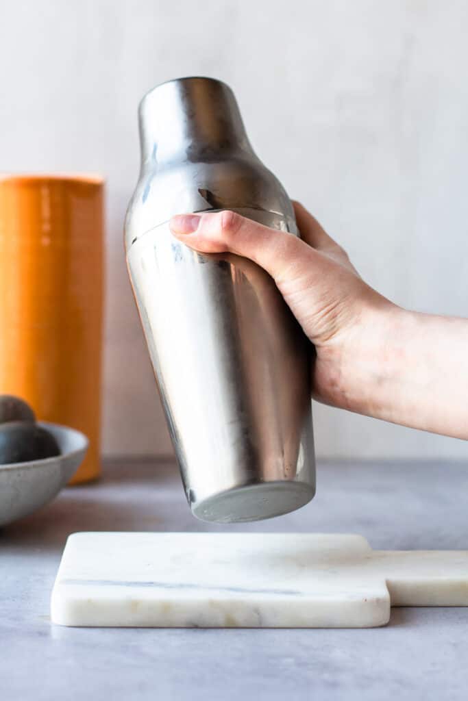 Hand shaking a stainless-steel cocktail shaker.