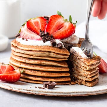 Fork stuck in a stack of protein pancakes decorated with yogurt and strawberries.