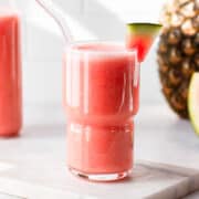 Watermelon smoothie in a glass with a whole pineapple in the background.