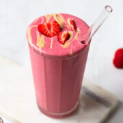 Pink smoothie with a drizzle of cashew butter and strawberries on top.