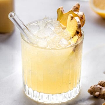 Yellow drink with lots of crushed ice, garnished with two slices of ginger root in a low-rise glass.