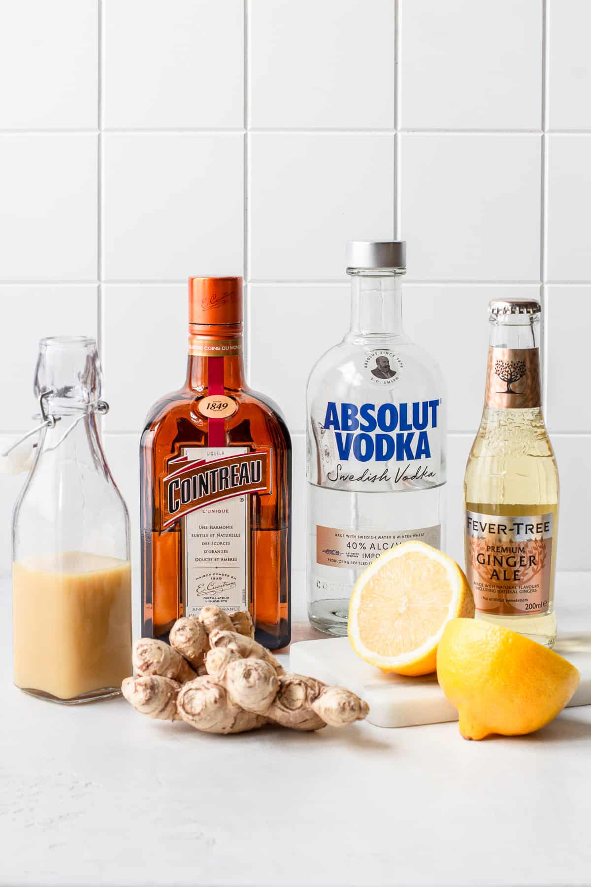 Alcohol bottles and mixers in front of a white tile background.