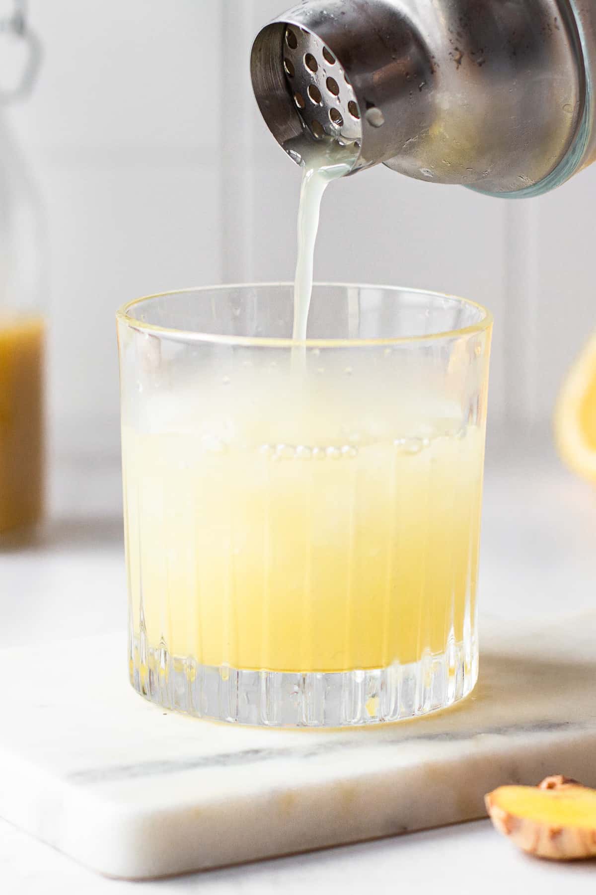 Hand pouring the mixed cocktail into a glass filled with ice.