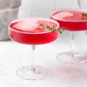 Pink cocktail in a coupe glass garnished with a sprig of thyme.