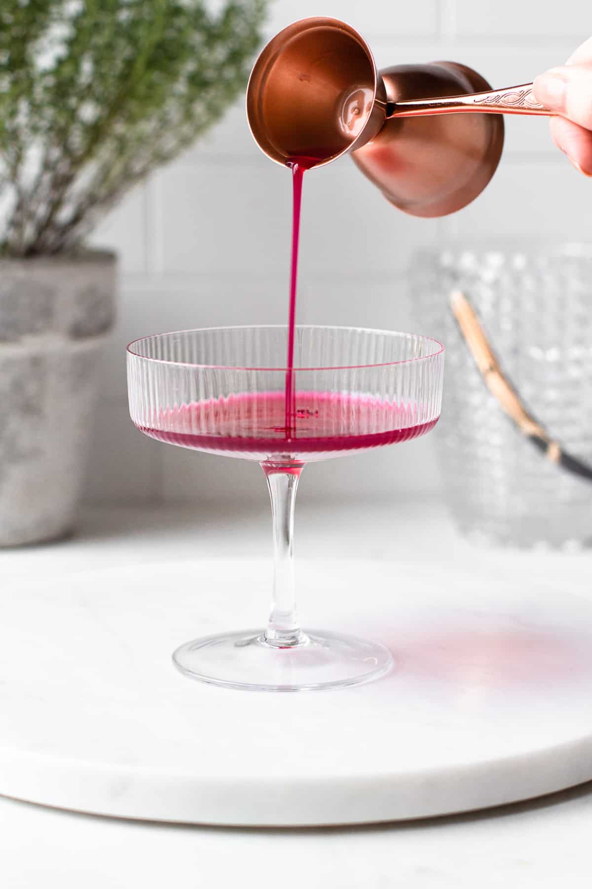 Hand pouring purple pomegranate juice into a coupe glass.