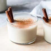 Coconut milk cocktail in a small glass jar garnished with a dash of cinnamon and two cinnamon sticks.