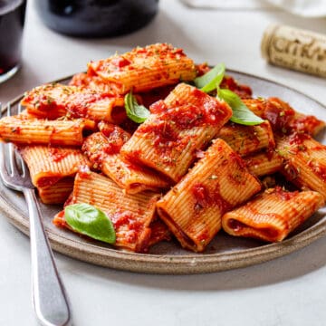 Grey ceramic plate filled with rigatoni covered in red sauce and topped with fresh basil.