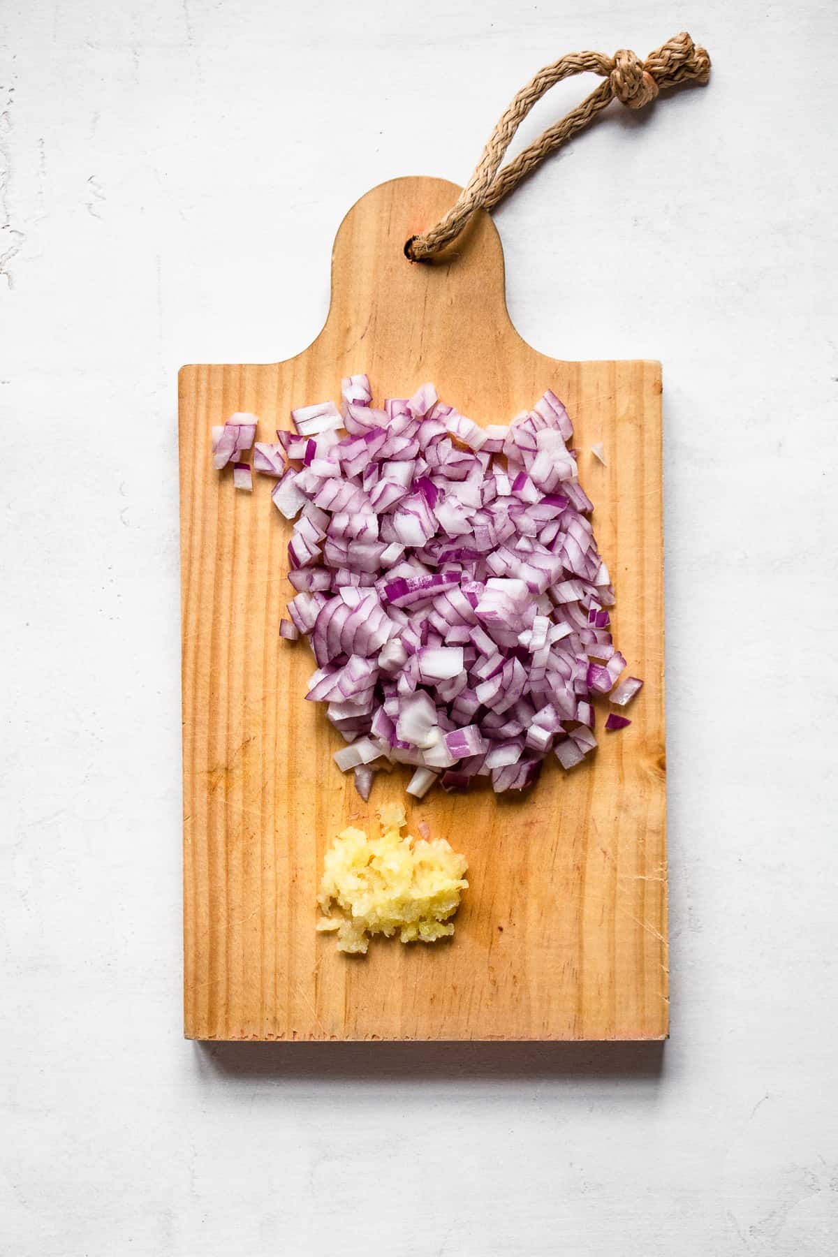 Minced red onion and garlic cloves on a wooden cutting board.