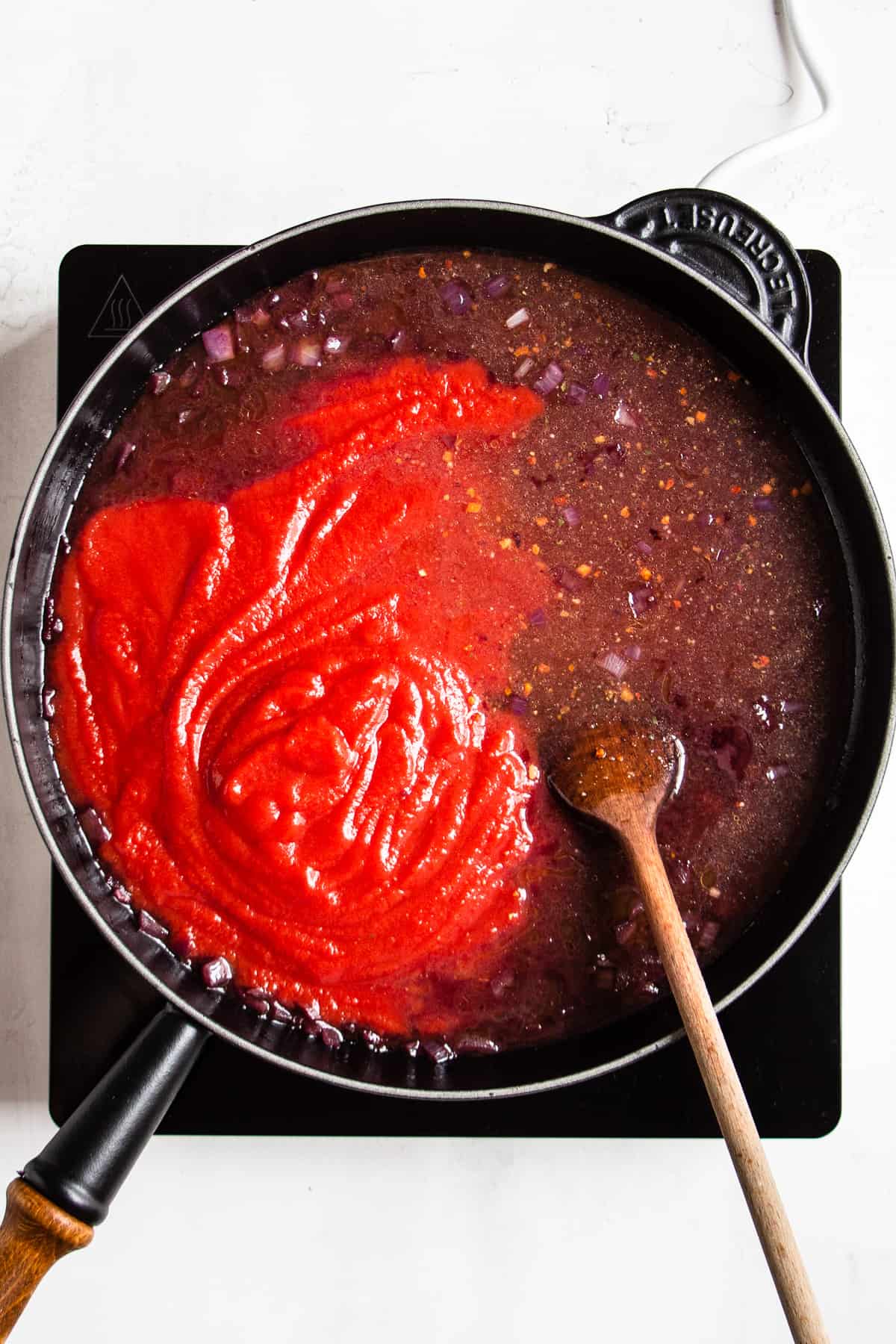 Passata and vegetable broth in a black pan.