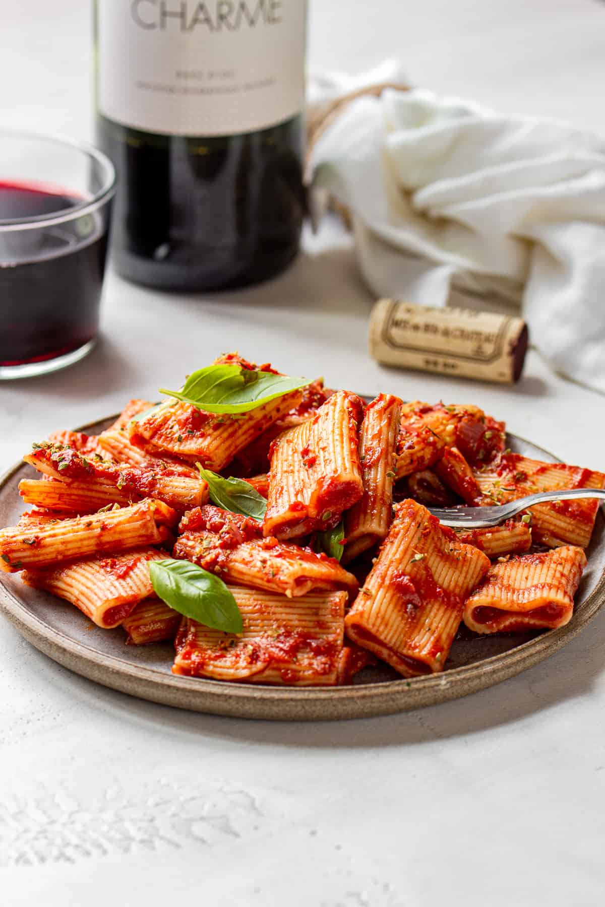 Plate with rigatoni in red sauce, a glass of wine and a wine cork.