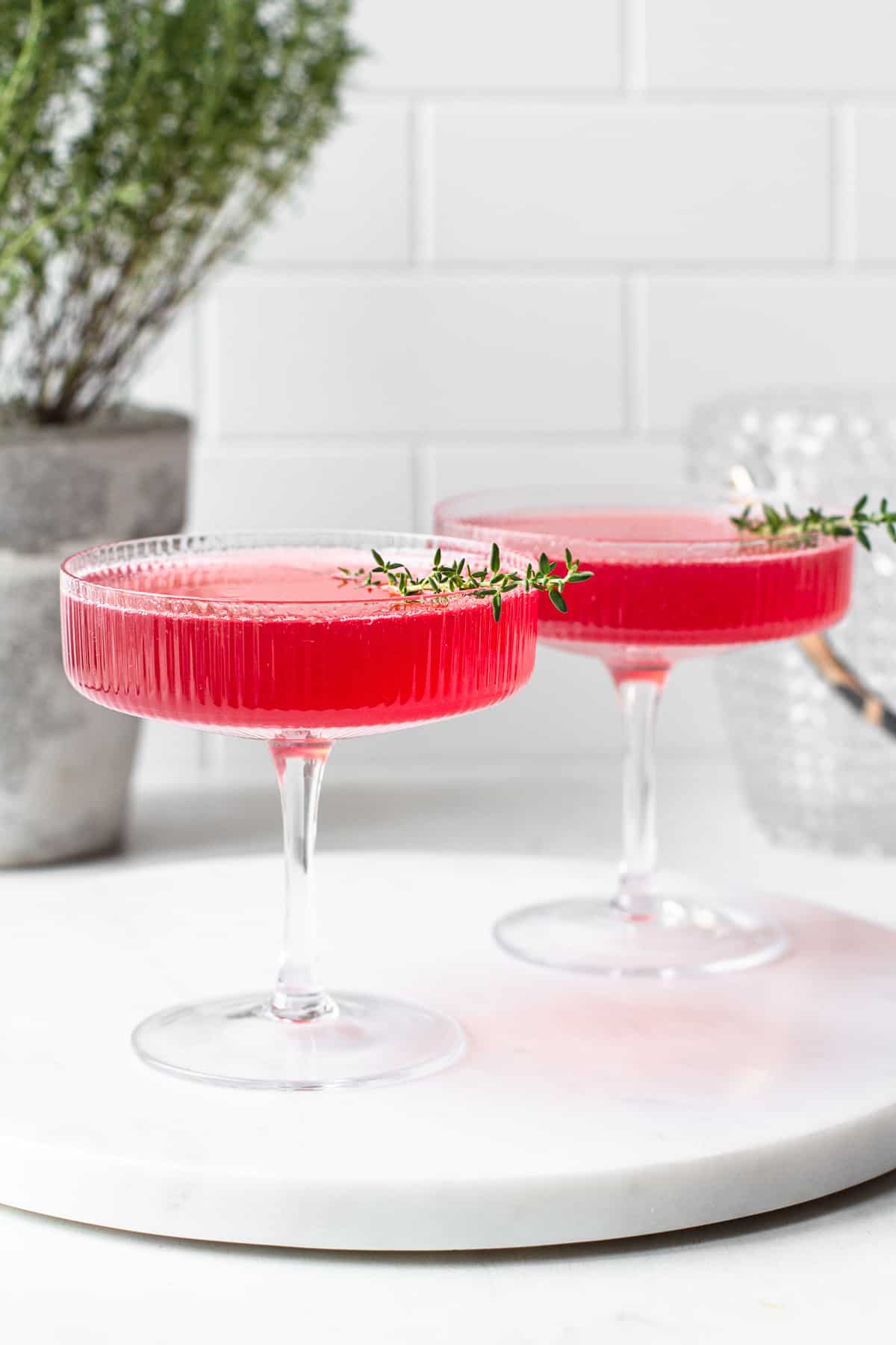 Pink cocktail in a champagne coupe glass in front of a white tile background.