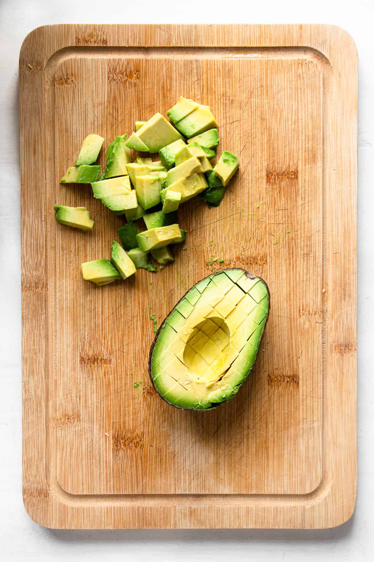 Pitted avocado and small avocado pieces on a wooden board.