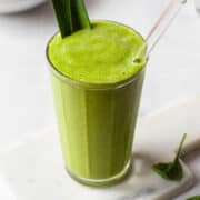 Green spinach smoothie in a ribbed glass jar with a glass straw.